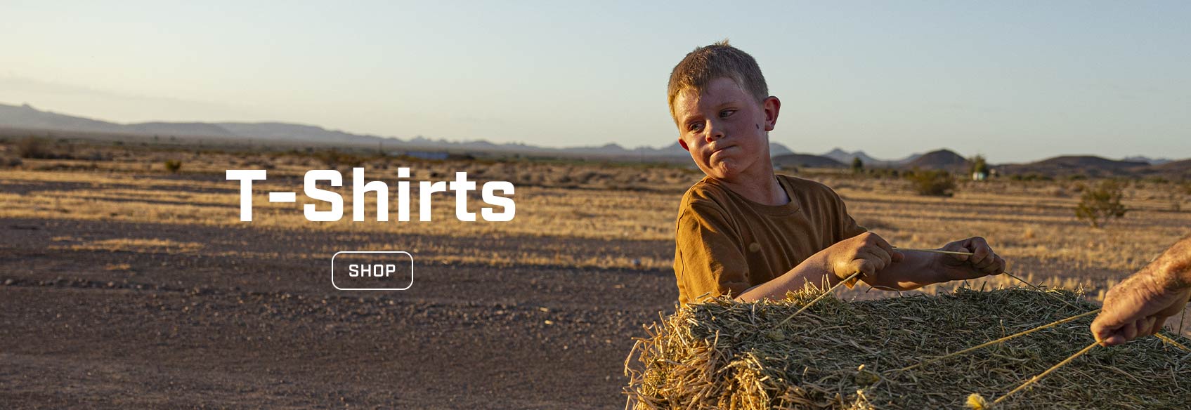 A young boy in a Carhartt t-shirt holding a bale of hay