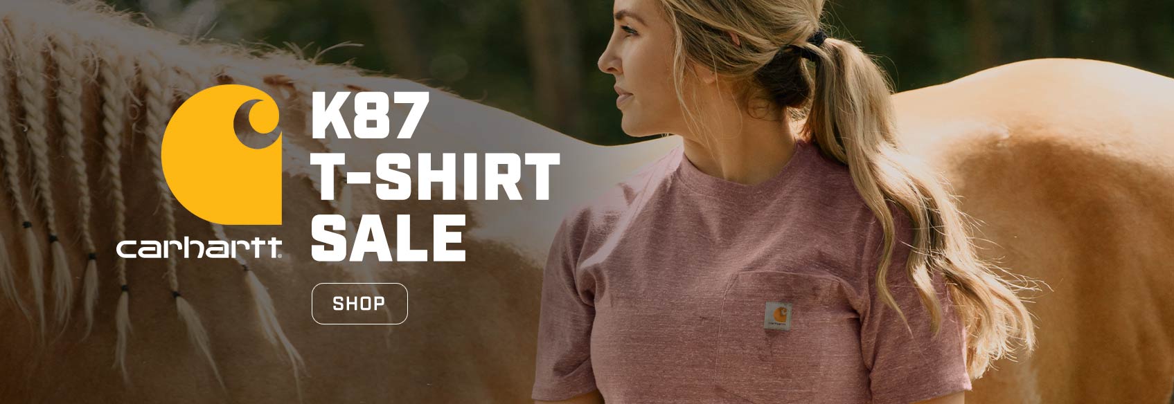 A woman wearing a carhartt t-shirt standing in front of a horse.