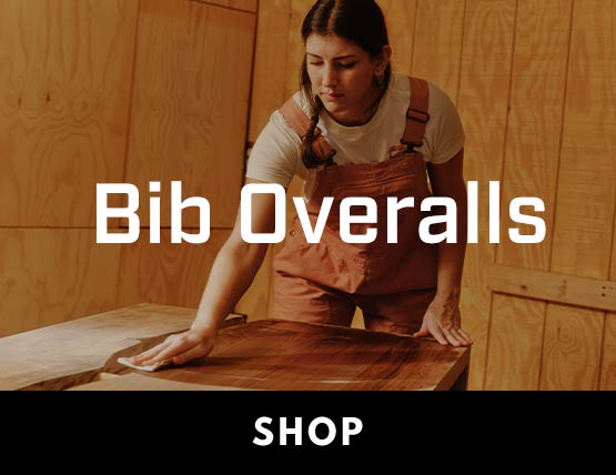 A woman staining a table in Carhartt bib overalls