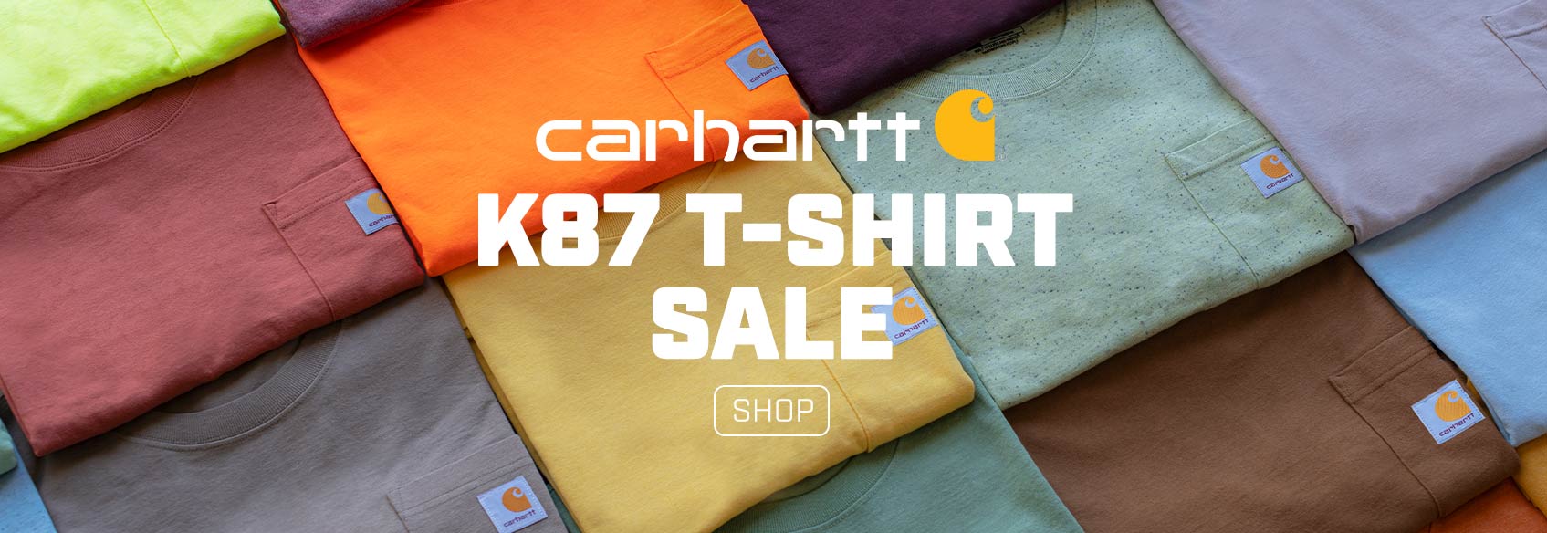 Over 15 folded Carhartt t-shirts sitting on the ground. 