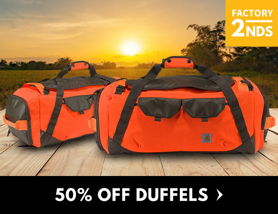 Two orange duffel bags sitting on a wood deck in front of  field. 