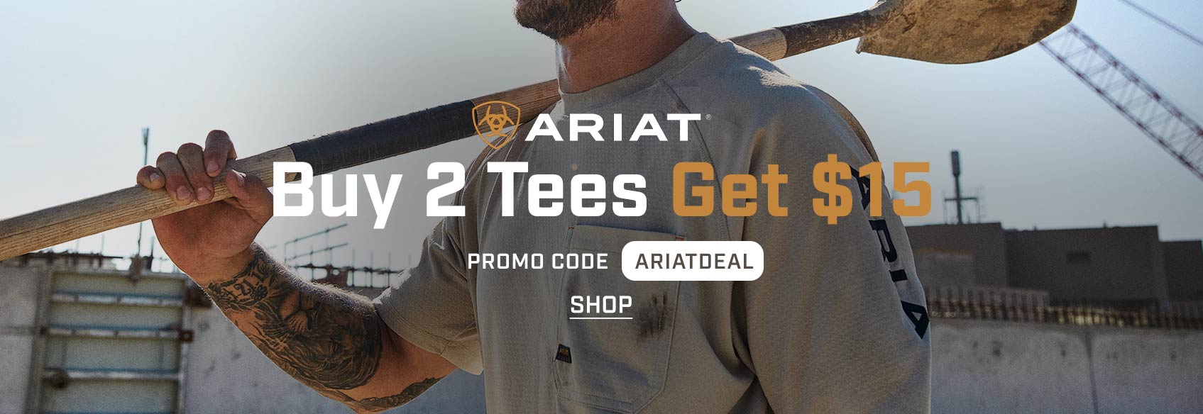A man wearing an Ariat t-shirt with a shovel over his shoulder. 