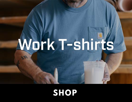 A man painting in his shop wearing a blue Carhartt t-shirt.