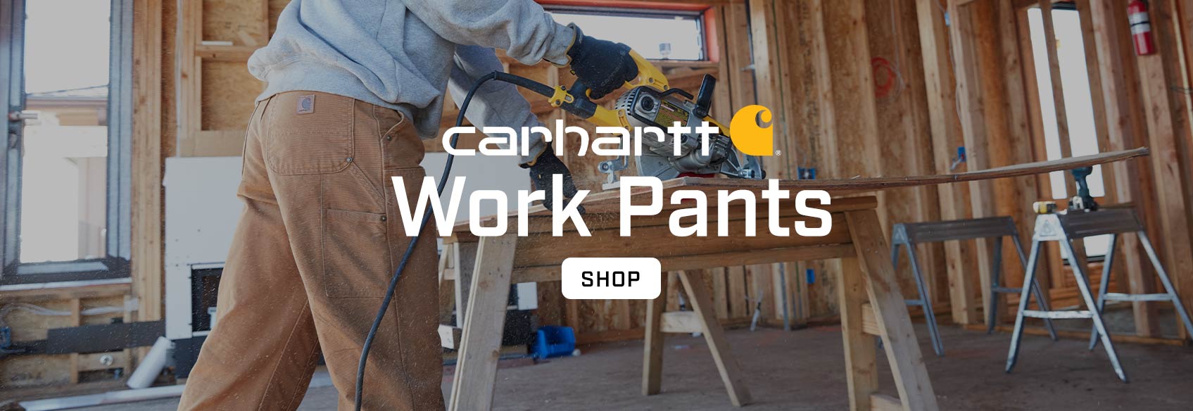 A carpenter sawing a board wearing Carhartt work pants