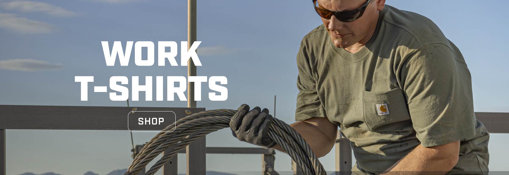 A man working outside wearing a Carhartt t-shirt and winding up steel cable.